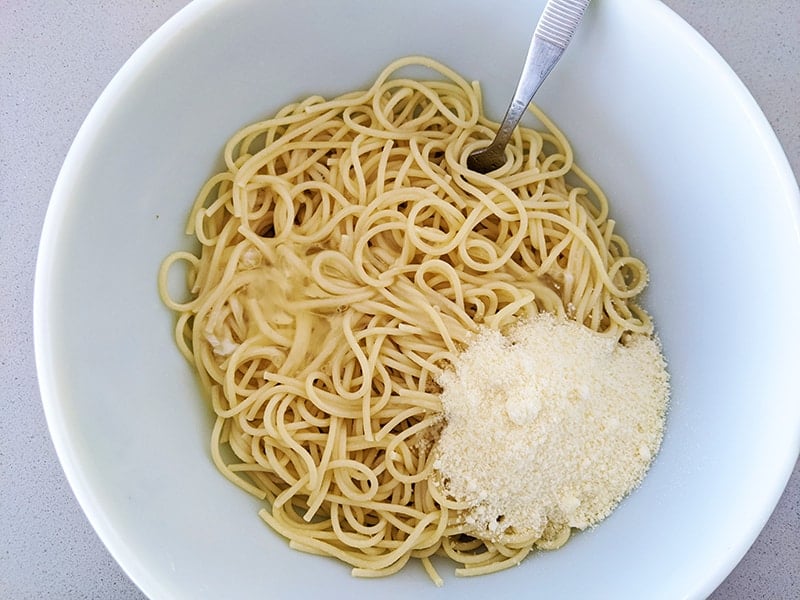 mixing cooked pasta with the eggs and Parmesan on a large white bowl