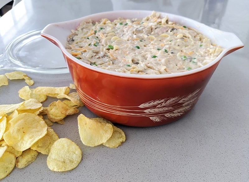 mixed pasta and tuna ingredients in Red Harvest Pyrex casserole ready for baking, pieces of potato chips on the side