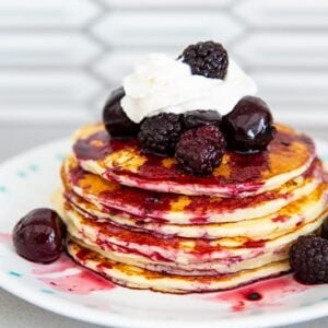 cottage cheese pancakes in a stack with whipped cream and blackberries, blueberries and cherries on top