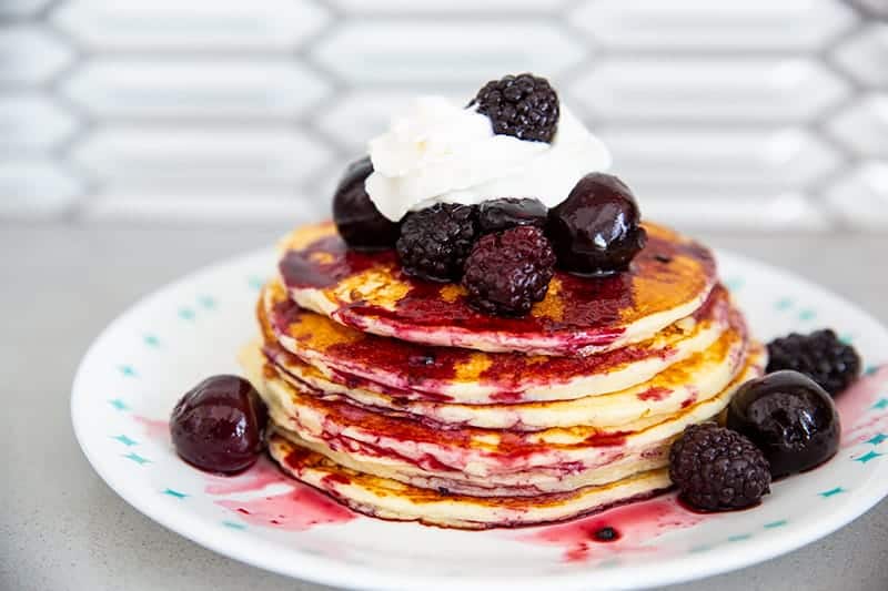 cottage cheese pancakes in a stack with whipped cream and blackberries, blueberries and cherries on top