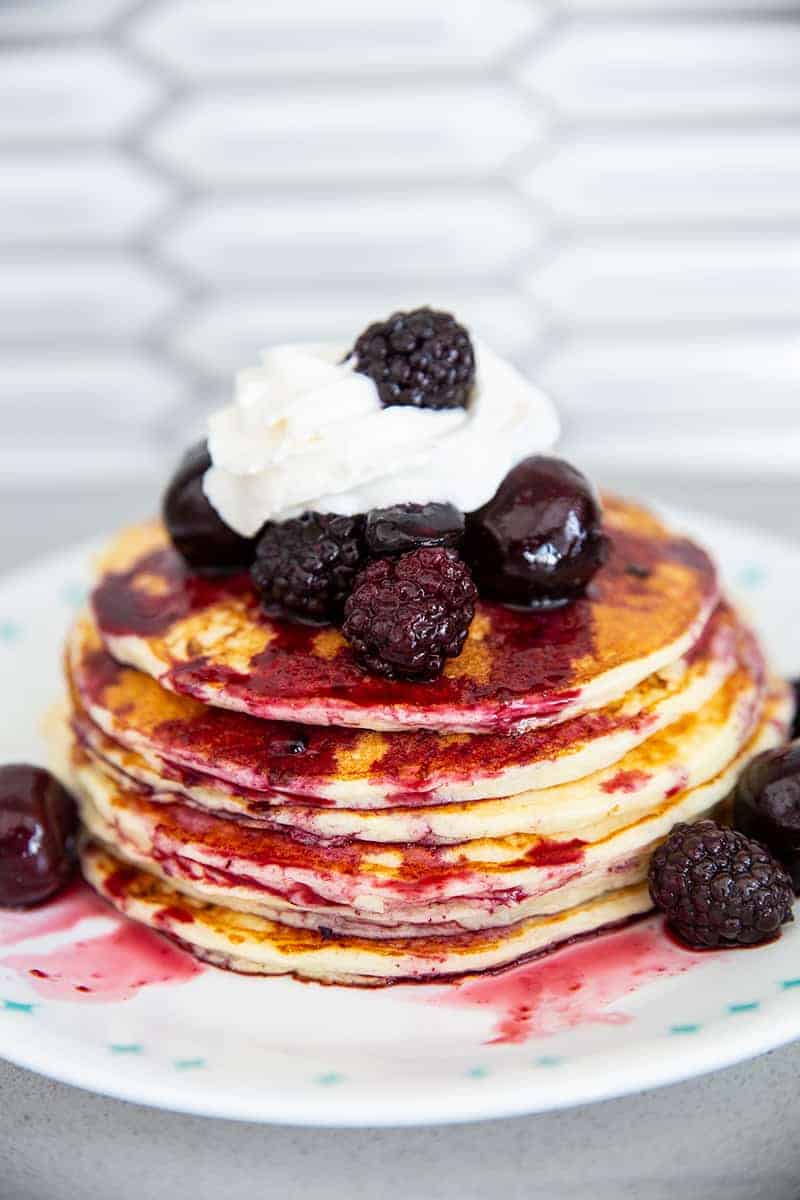 cottage cheese pancakes in a stack with whipped cream and blackberries, blueberries and cherries on top