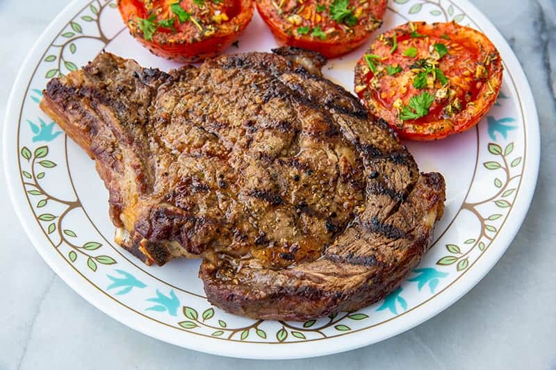 grilled rib eye steak on a white plate with tomatoes 