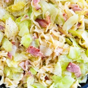 close up of cabbage, onions and noodles with bacon in a black frying pan