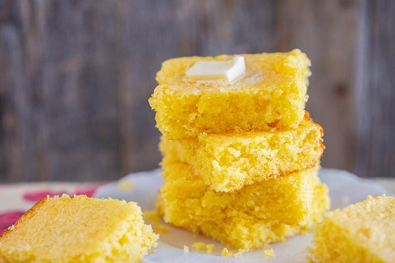 a stack of Jiffy cornbread slices with melting butter on top on a white plate