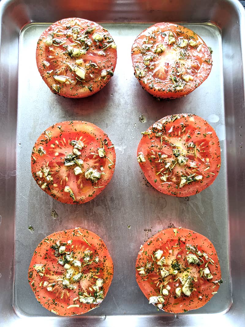 close up of oven roasted tomatoes on a sheet pan loaded with garlic and herbs