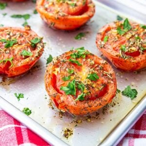 roasted tomatoes on a sheet pan with red kitchen towel underneath