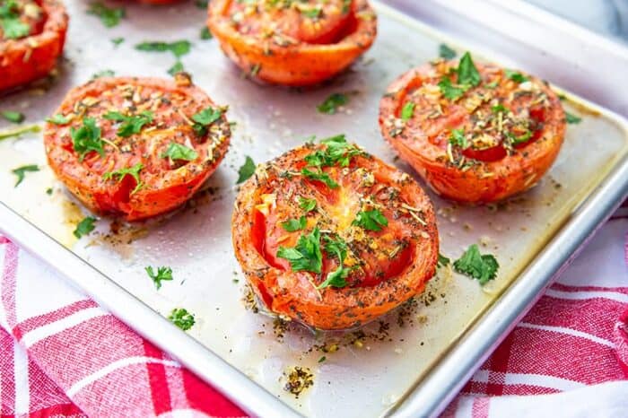 roasted tomatoes on a sheet pan with red kitchen towel underneath