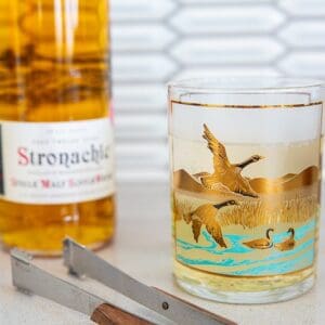 scotch bottle with ice tongs and a vintage Canada goose glass with scotch and soda in it