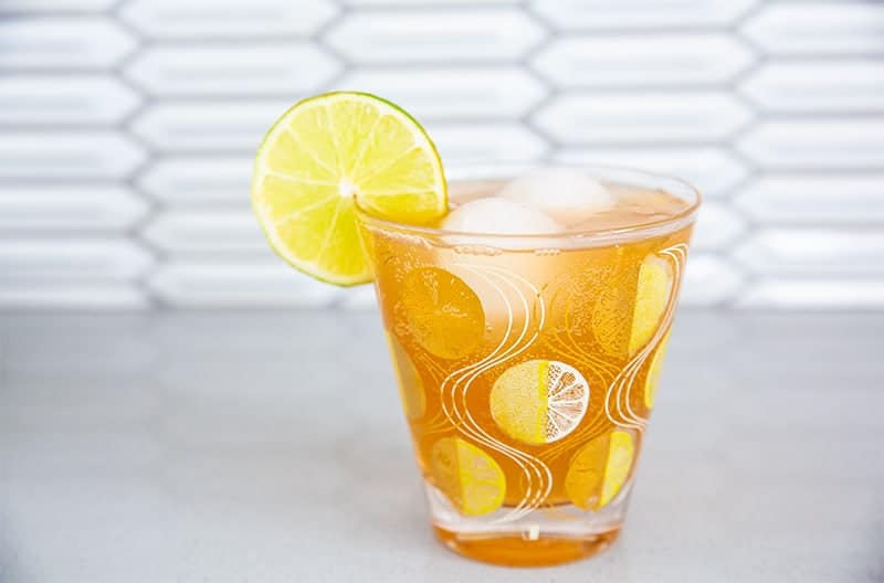 a suffering bastard cocktail in a stunning glass with gold emblazoned garnished with a lemon wedge on the side