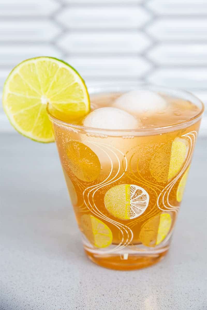 a suffering bastard cocktail in a stunning glass with gold emblazoned garnished with a lemon wedge on the side
