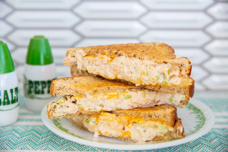 cheesy tuna melt sandwich pieces stacked on top of each other on a white plate with salt and pepper shakers at the side