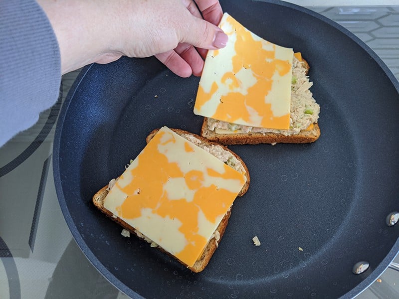 two slices of grainy bread on a large skillet each with tuna fillings and cheese slice