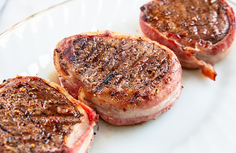 three pieces filet mignon wrapped in bacon on a white plate 