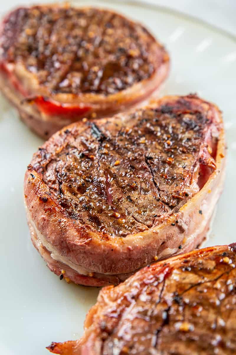 close up of a filet mignon steak wrapped in bacon on a white plate 