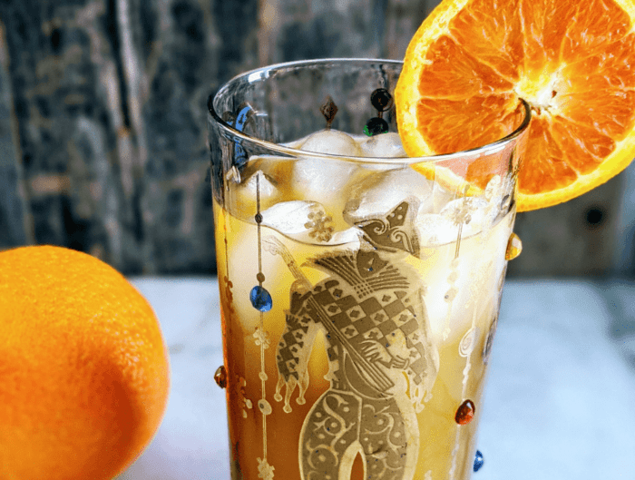 Close up of a Brass Monkey Cocktail in a mardis gras style glass garnished with an orange