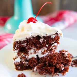 a slice of chocolate soda cake on a white plate with a piece of red cherry on top