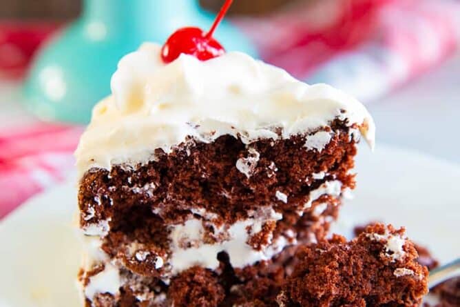 a slice of chocolate soda cake on a white plate with a piece of red cherry on top