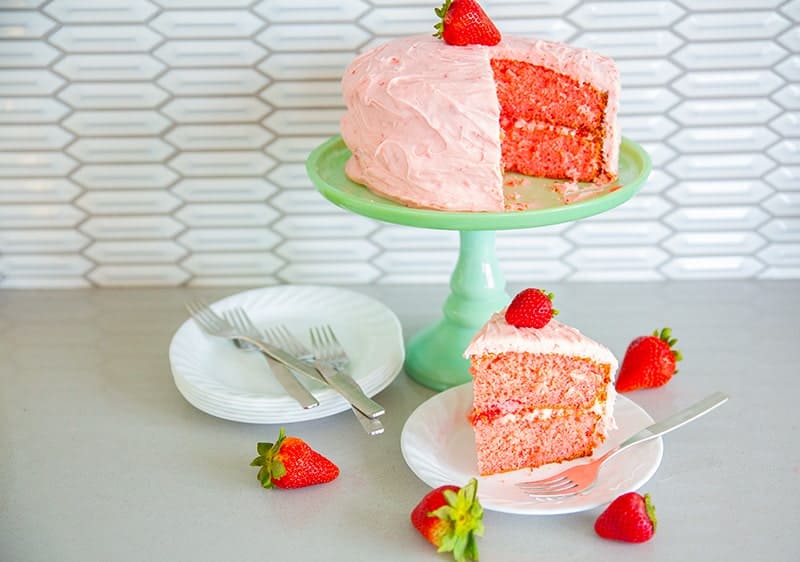 strawberry cake on a jadeite cake stand with fresh strawberries, white plates and forks 