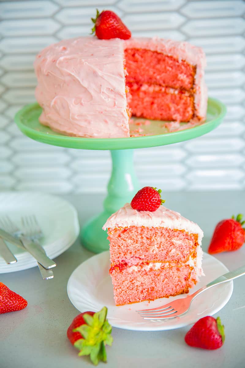 strawberry cake on a jadeite cake stand with strawberries, white plates and forks 