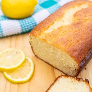lemon bread sitting on a wooden board with lemons and a turquoise kitchen towel