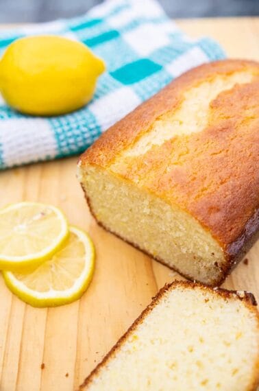 lemon bread sitting on a wooden board with lemons and a turquoise kitchen towel