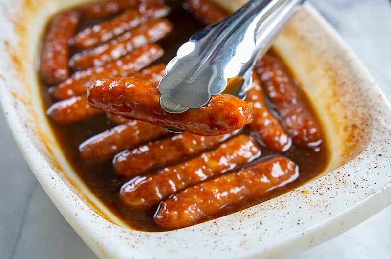 breakfast sausages in a white Pyrex baking dish being held with metal tongs