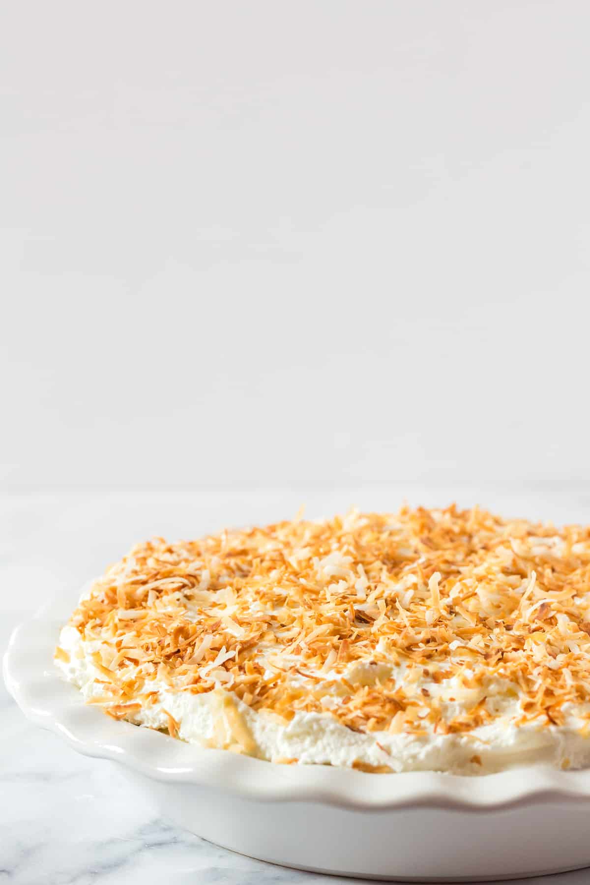 close up coconut cream pie in a white pie plate