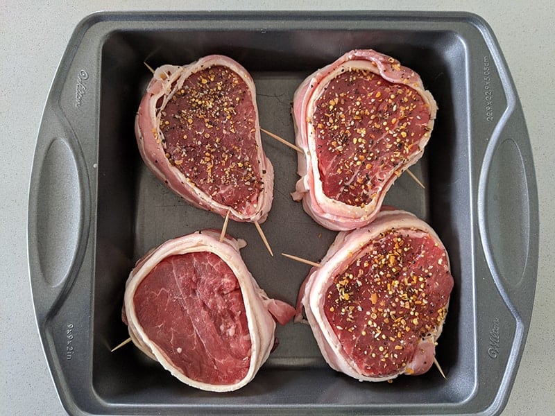 raw filet mignon steaks wrapped in raw bacon, secured with toothpicks and seasoned with steak seasoning