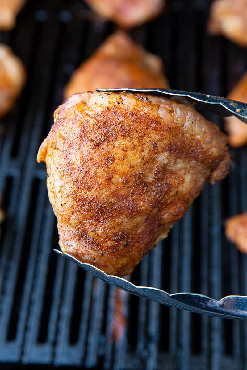 tongs holding a piece of cooked grilled chicken thigh