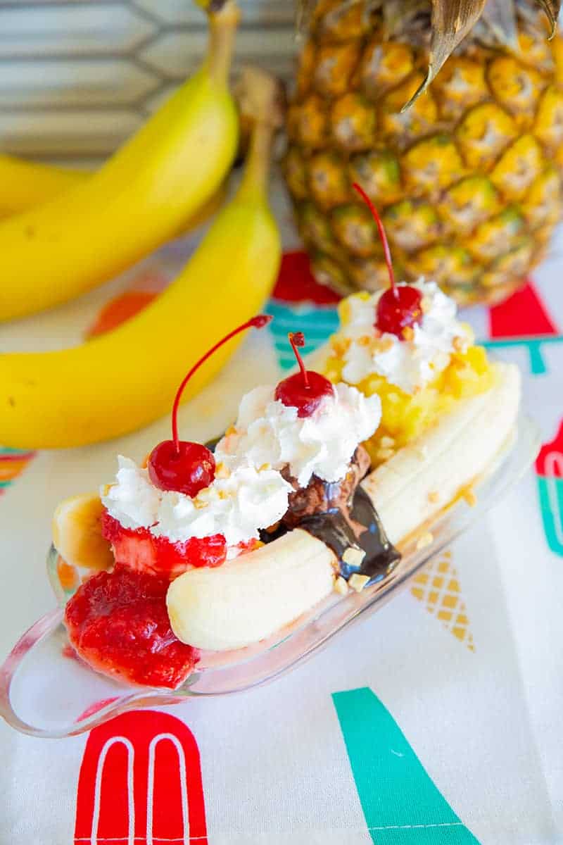 Ice Cream Banana Split on a banana boat dish, ripe banana and pineapple on background 