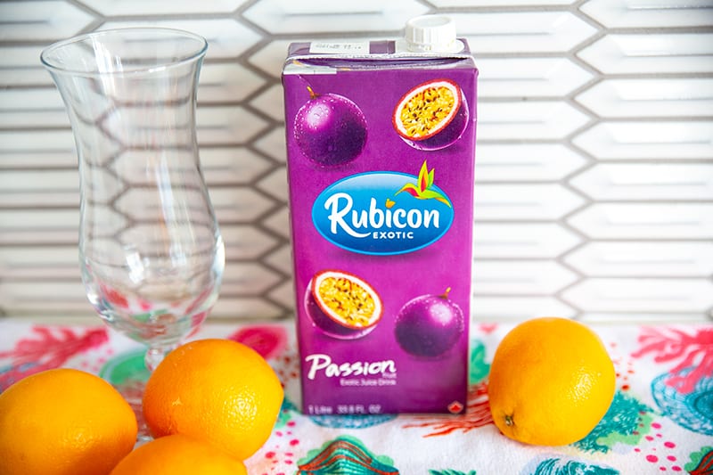 A container of passion fruit juice on a counter surrounded by oranges