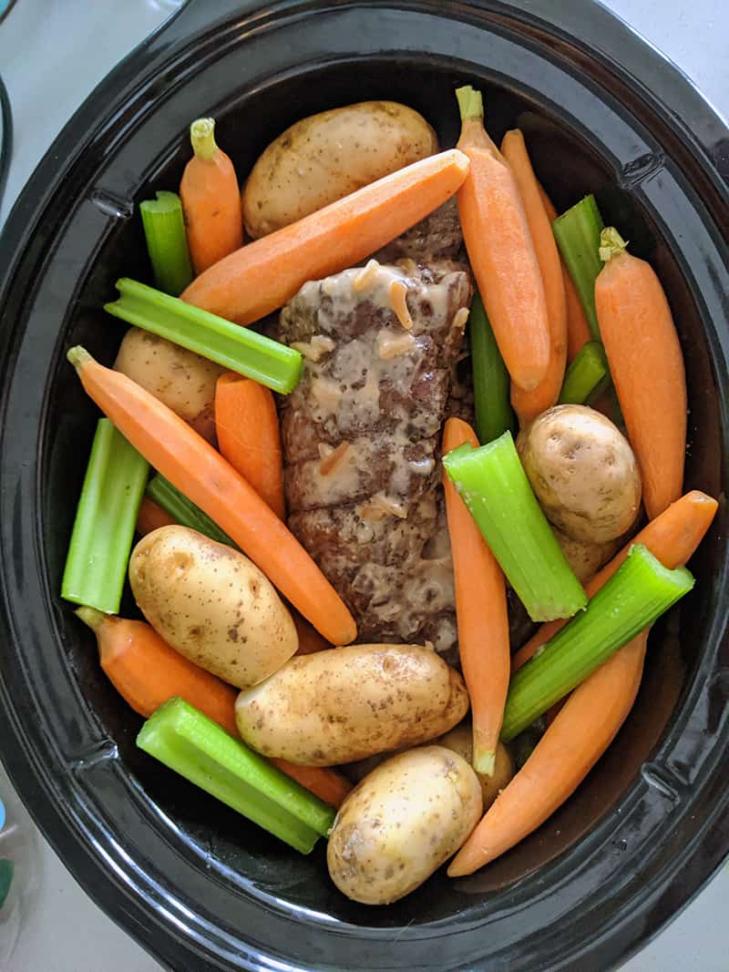 por roast and raw vegetables in a slow cooker