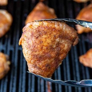 tongs holding a piece of cooked grilled chicken thigh