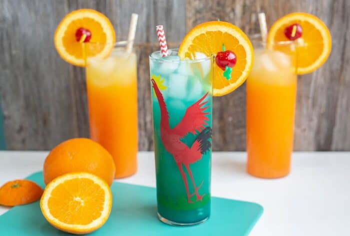Green Screwdriver served up in a red rooster glass with orange slice and cherry on a white counter