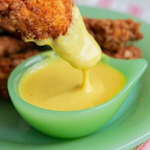 Chicken Strip dipping into a container of honey mustard sauce