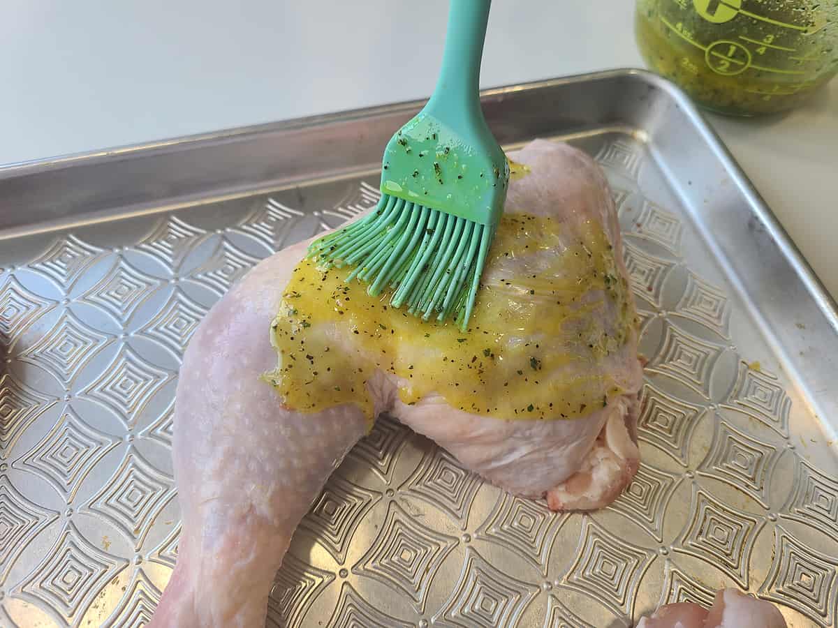 Brushing the sauce over a piece of chicken leg quarter