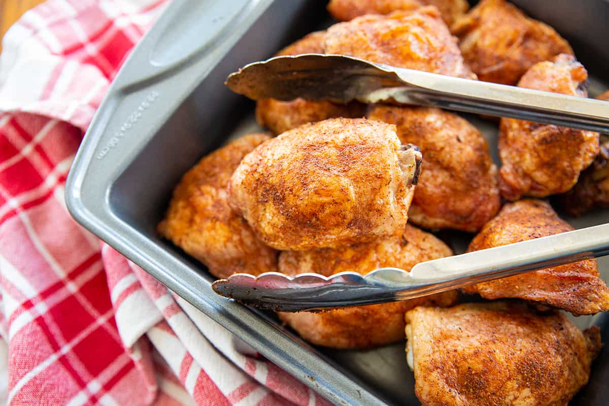 grilled chicken thighs and a kitchen tong on a baking pan