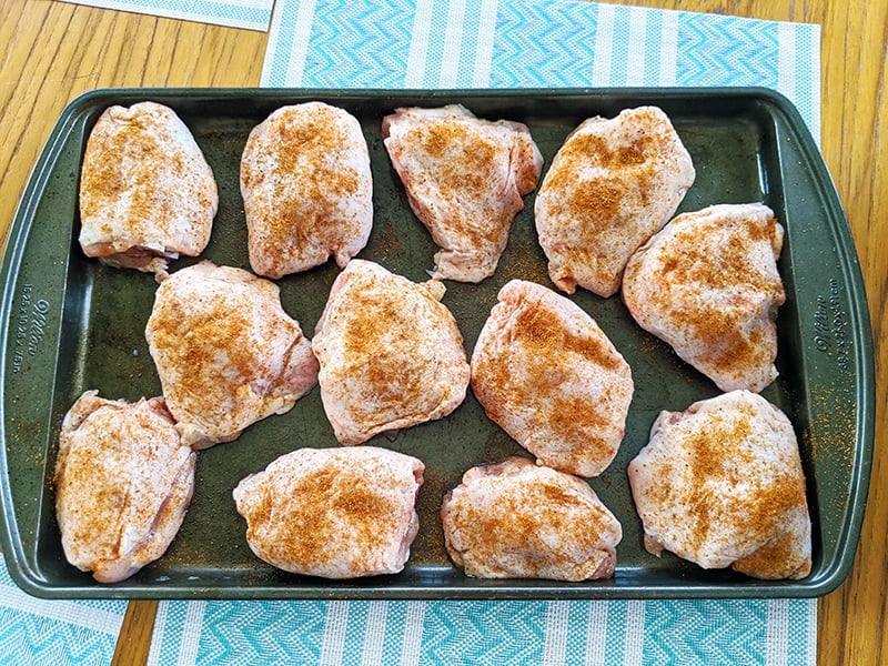 baking pan with raw, seasoned coated chicken thighs