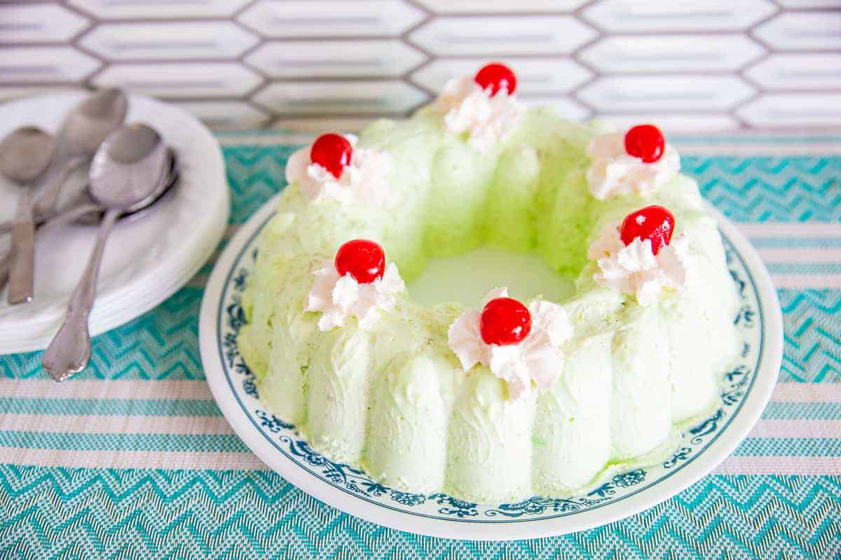 Seafoam Salad topped with Whipped Cream and Red Cherries, stack of plates and spoons on the side