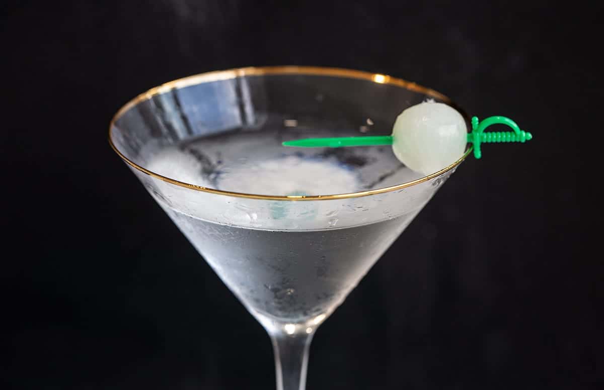 Gibson Cocktail on a black background garnished with a pickled onion 