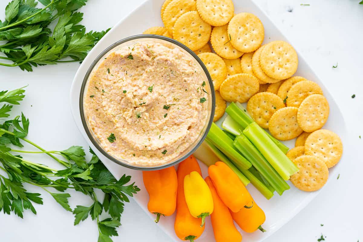 Top down shot of ham salad in a bowl surrounded by celery, peppers and crackers