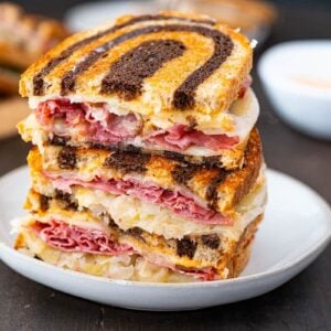 Reuben Sandwich on a white plate with russian dressing in the background