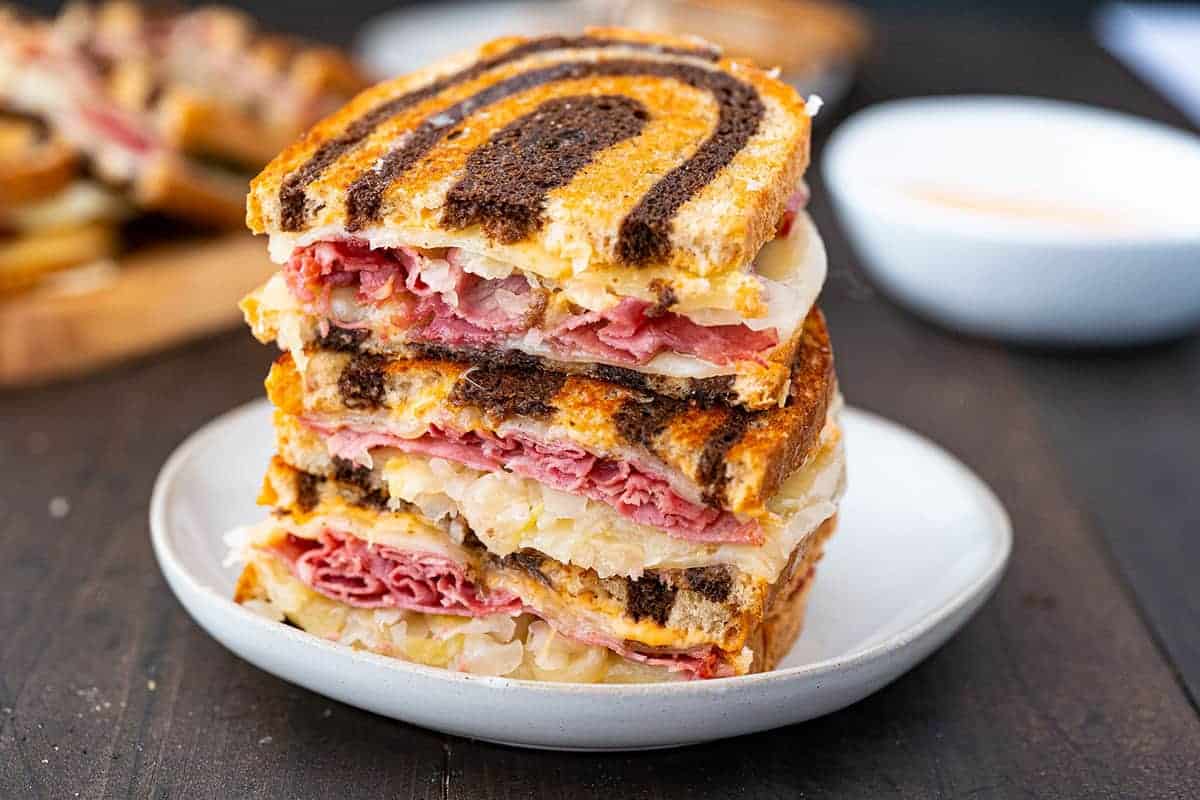 Reuben Sandwich on a white plate with russian dressing in the background