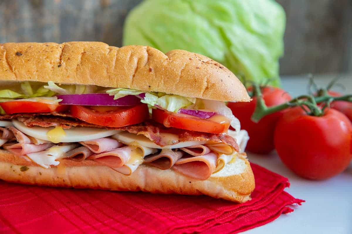 Submarine Sandwich on a red napkin with tomatoes and lettuce.