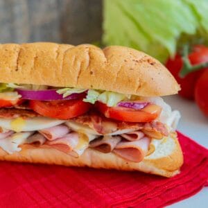 close up Submarine Sandwich on a red napkin with tomatoes and lettuce.