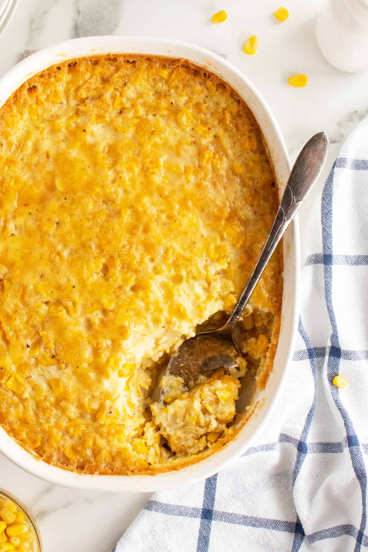 creamy corn pudding in a white casserole dish with a spoonful out of it