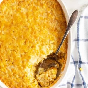 creamy corn pudding in a white casserole dish with a spoonful out of it