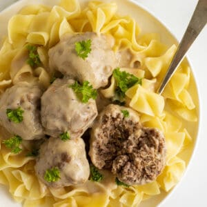 creamy swedish meatballs on a white plate with a sliced meatball