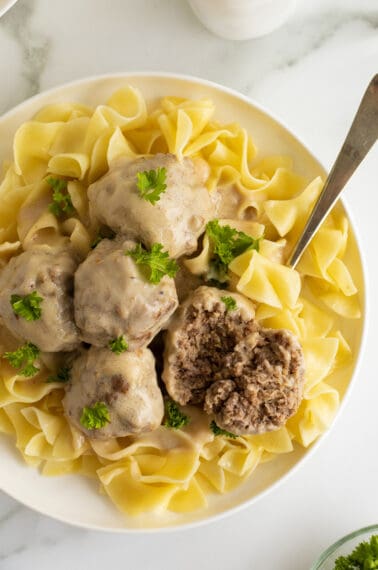 creamy swedish meatballs on a white plate with a sliced meatball