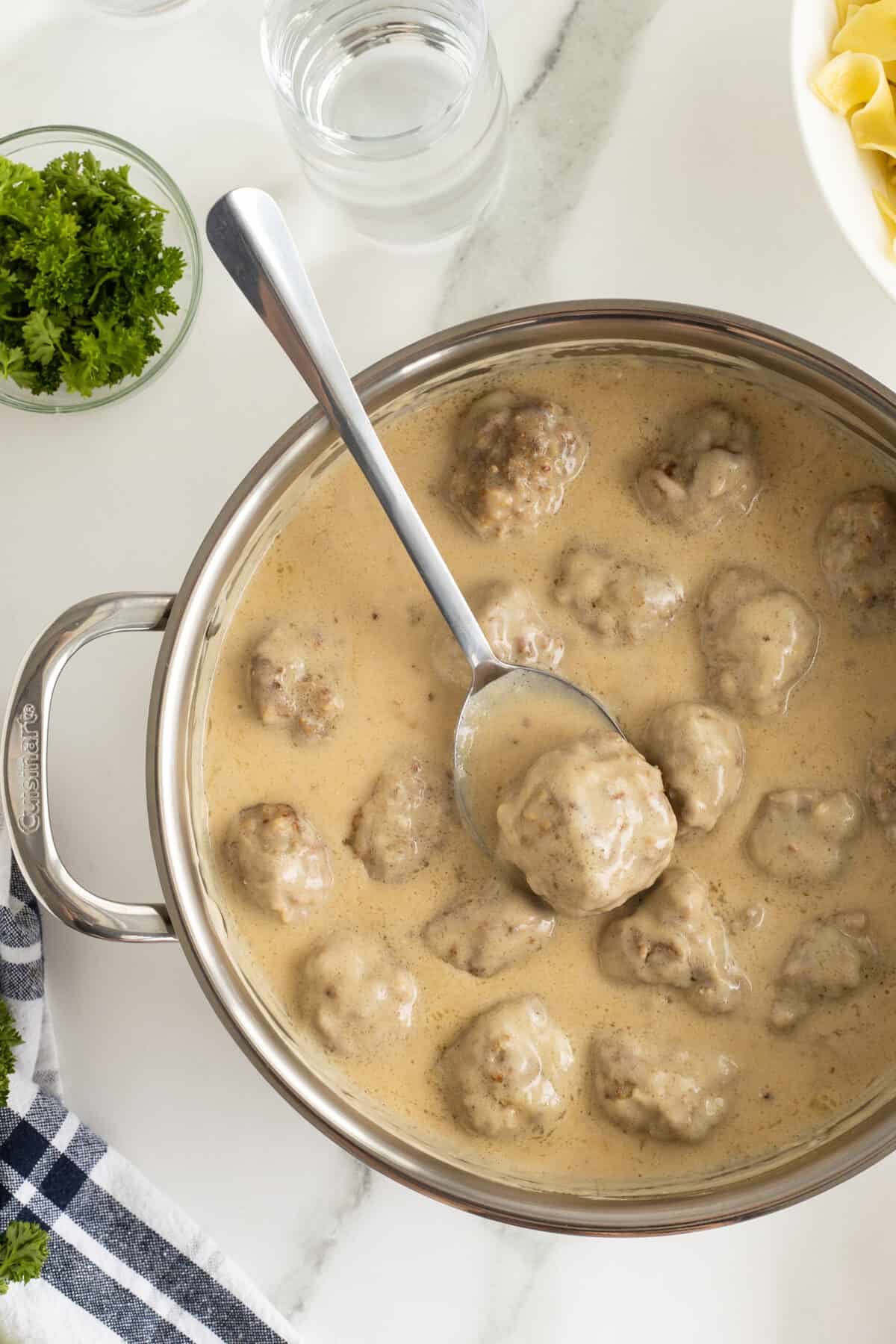 creamy swedish meatballs in a pot with a wooden spoon with a meatball on it